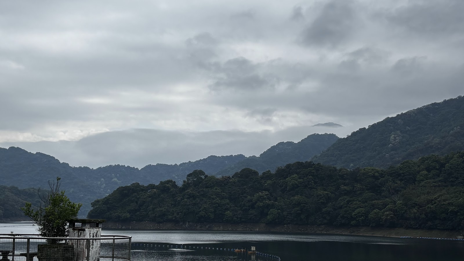 石門水庫陰天水面廣闊，山巒在霧中若隱若現，左側有水閘構建物