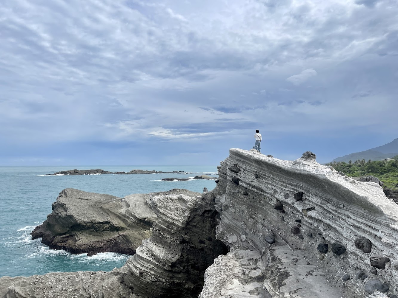 海岸岩石上一人遠望海洋與山巒