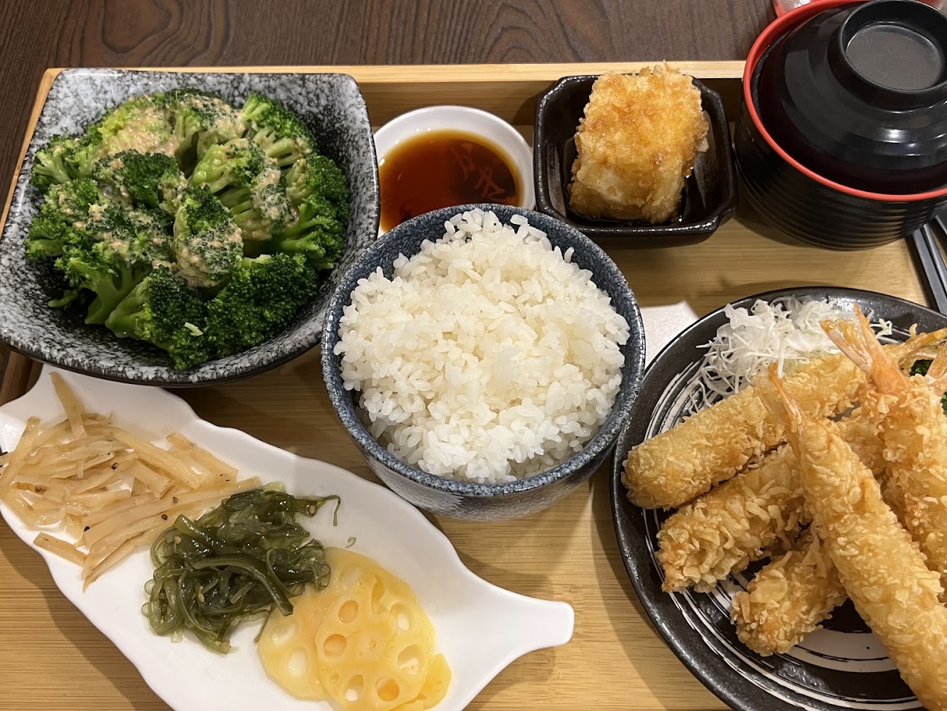 這張圖片展示了一份日式定食套餐，有炸蝦天婦羅、白飯、味噌湯、涼拌蔬菜、炸豆腐、涼拌花椰菜及醬料，看起來豐盛美味。