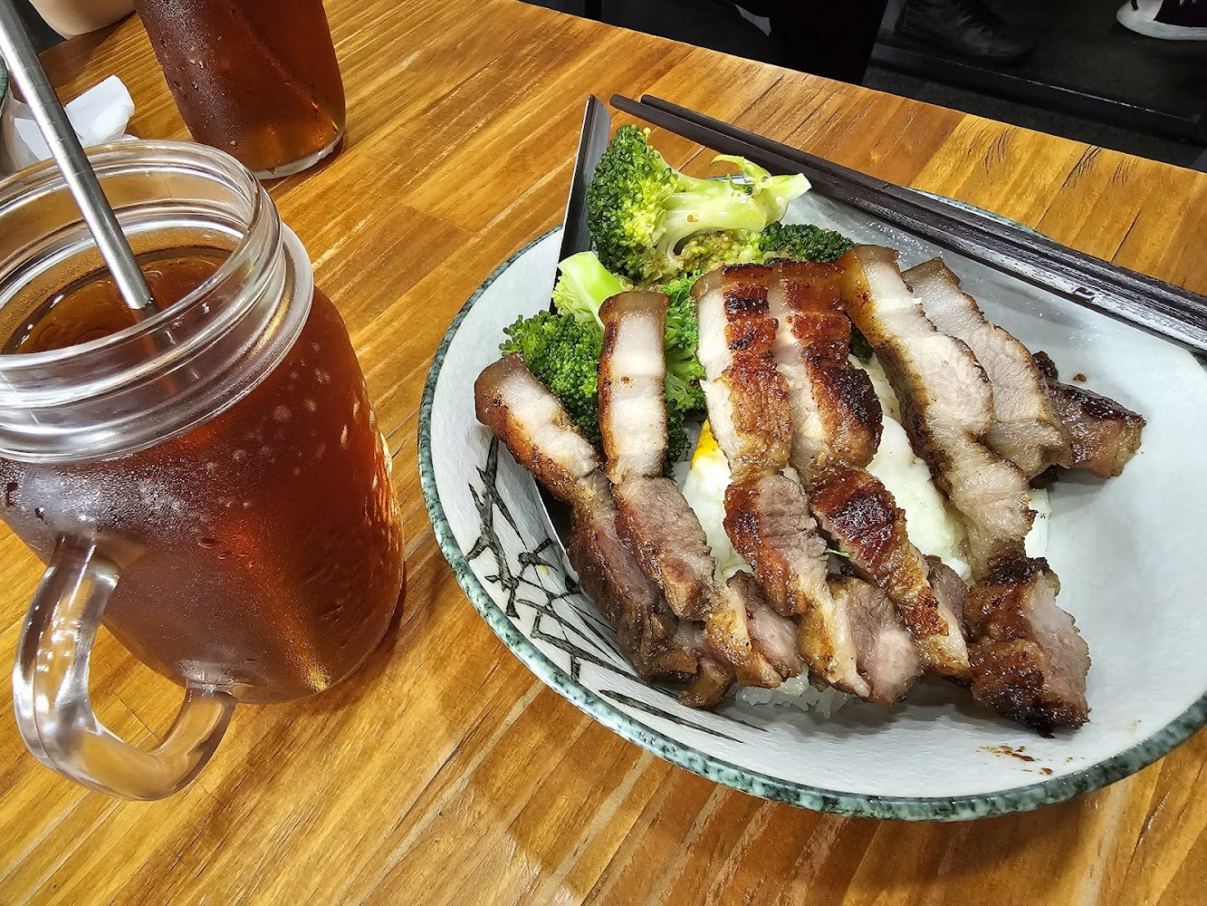 以烤豬肉為主的丼飯，配有白飯和花椰菜，旁邊有一杯冰紅茶