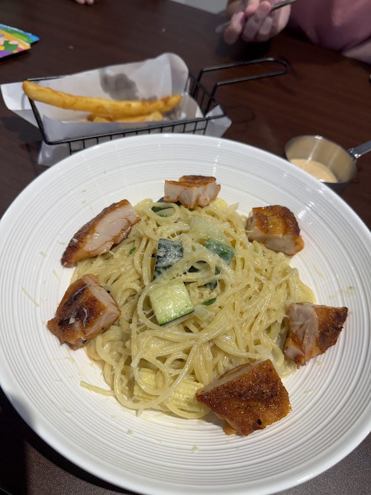 奶油義大利麵上放有多塊香煎雞肉，旁邊有炸物與沾醬