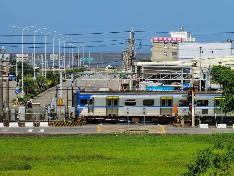 藍銀色火車經過平交道與綠地景色