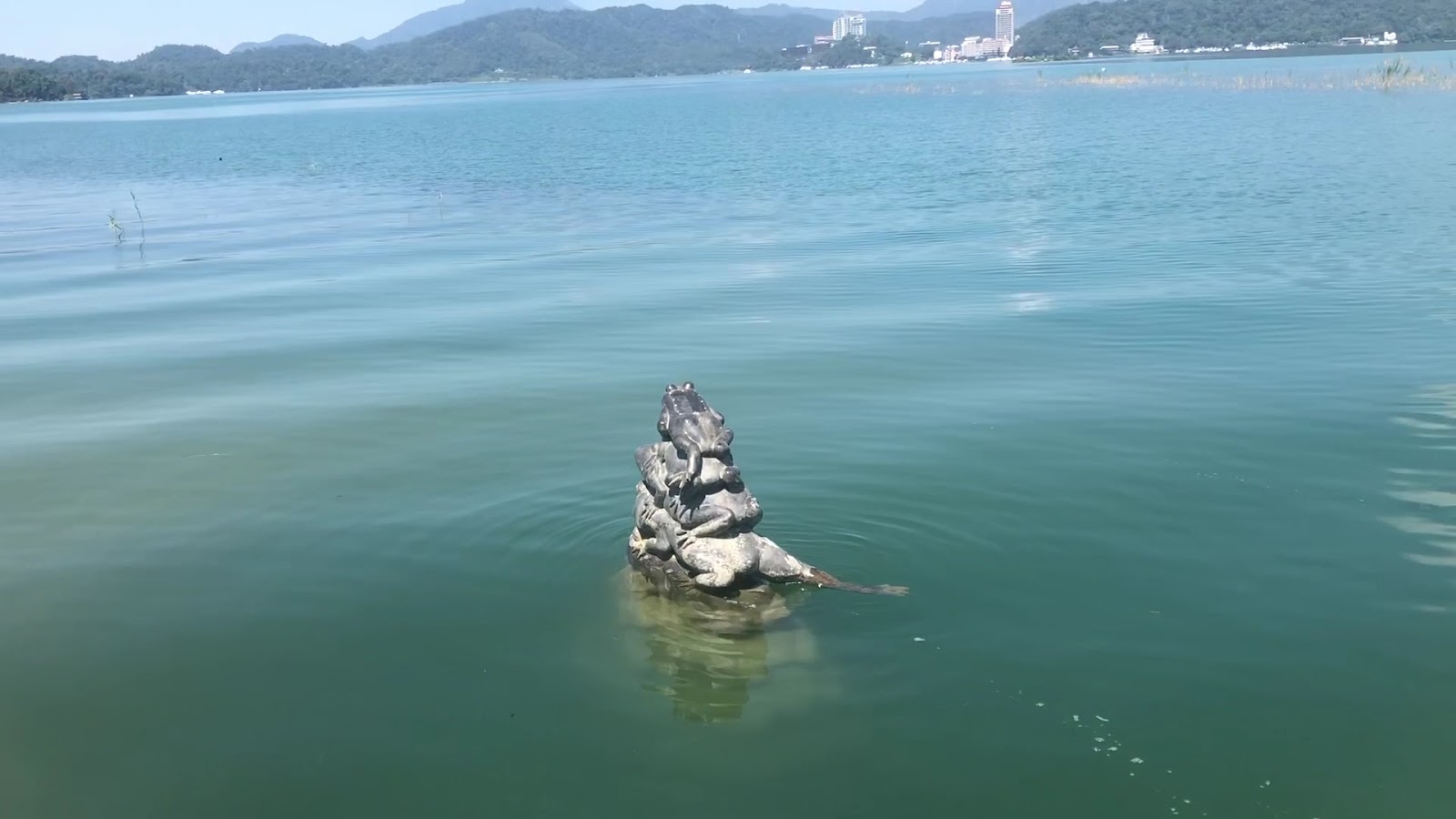 九蛙疊像全景，石雕立於日月潭湖中央，背景為湖水山脈與水社村建築