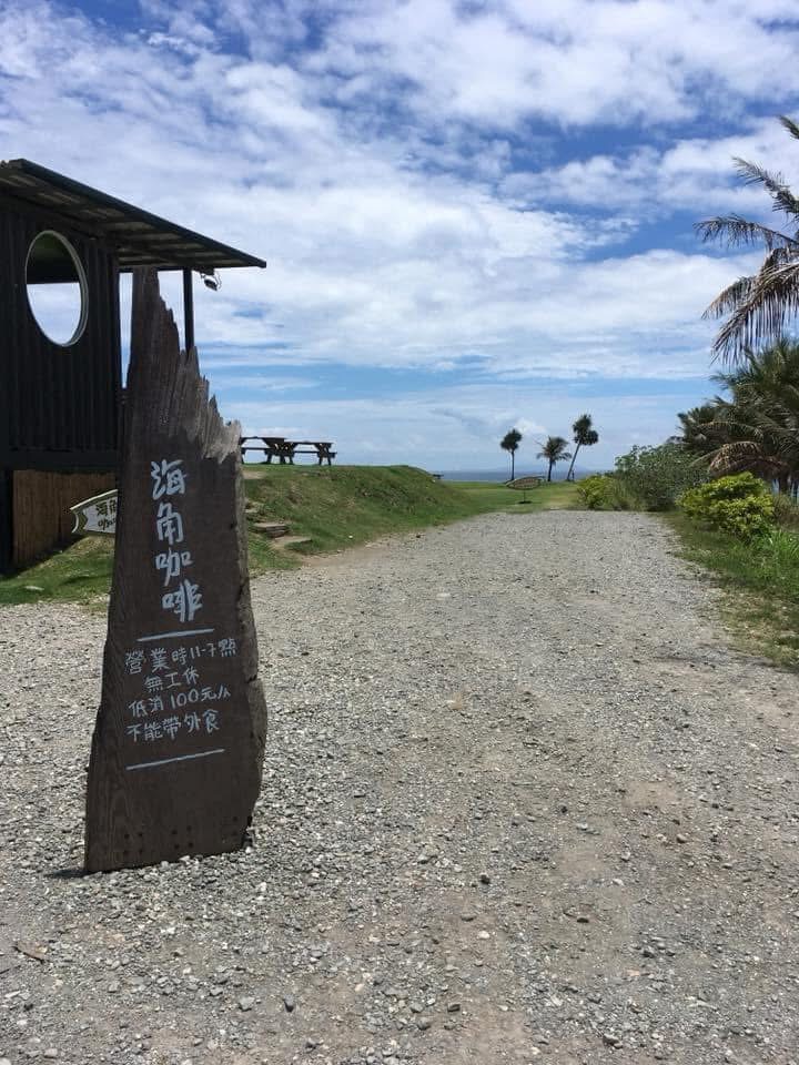 海邊咖啡館門口有木製招牌，遠方可見椰子樹與大海