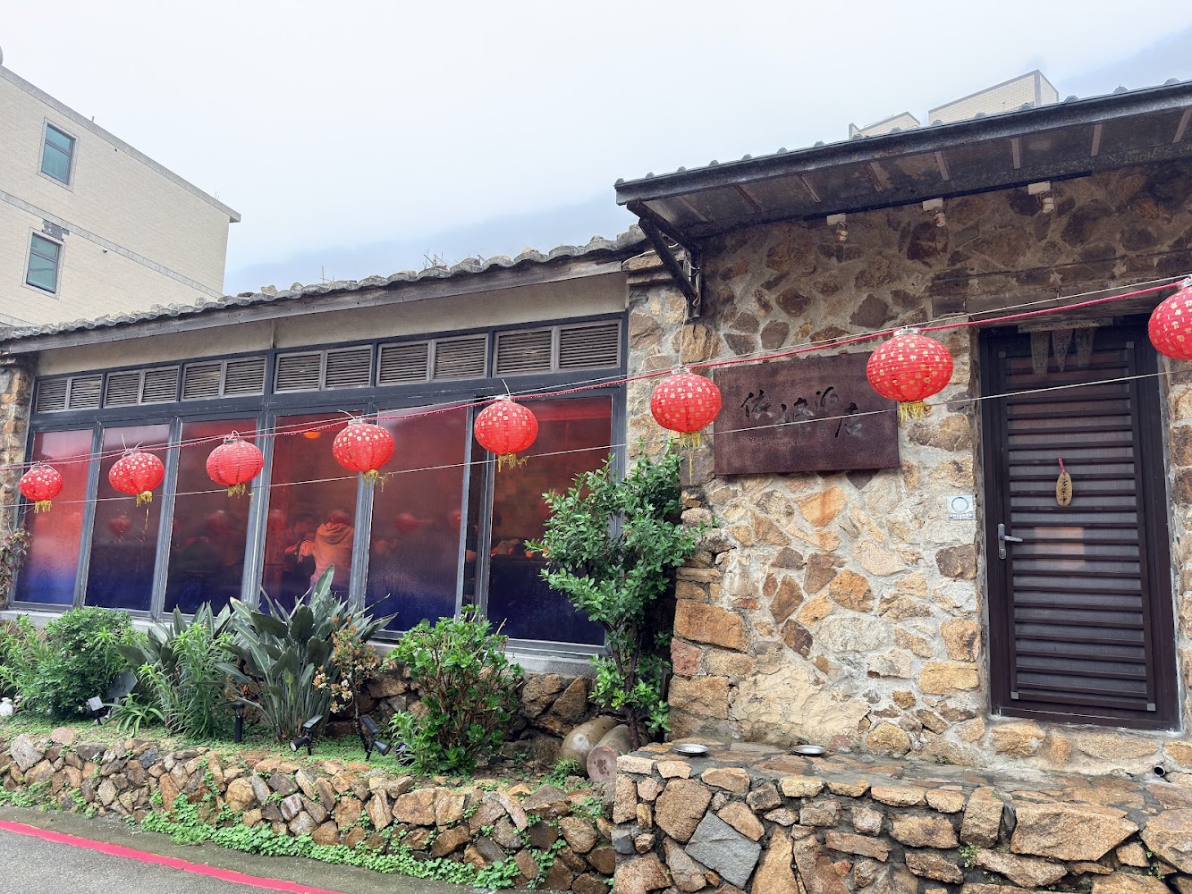 石頭建造的依嬤的店外觀，門口掛著木製招牌與紅燈籠