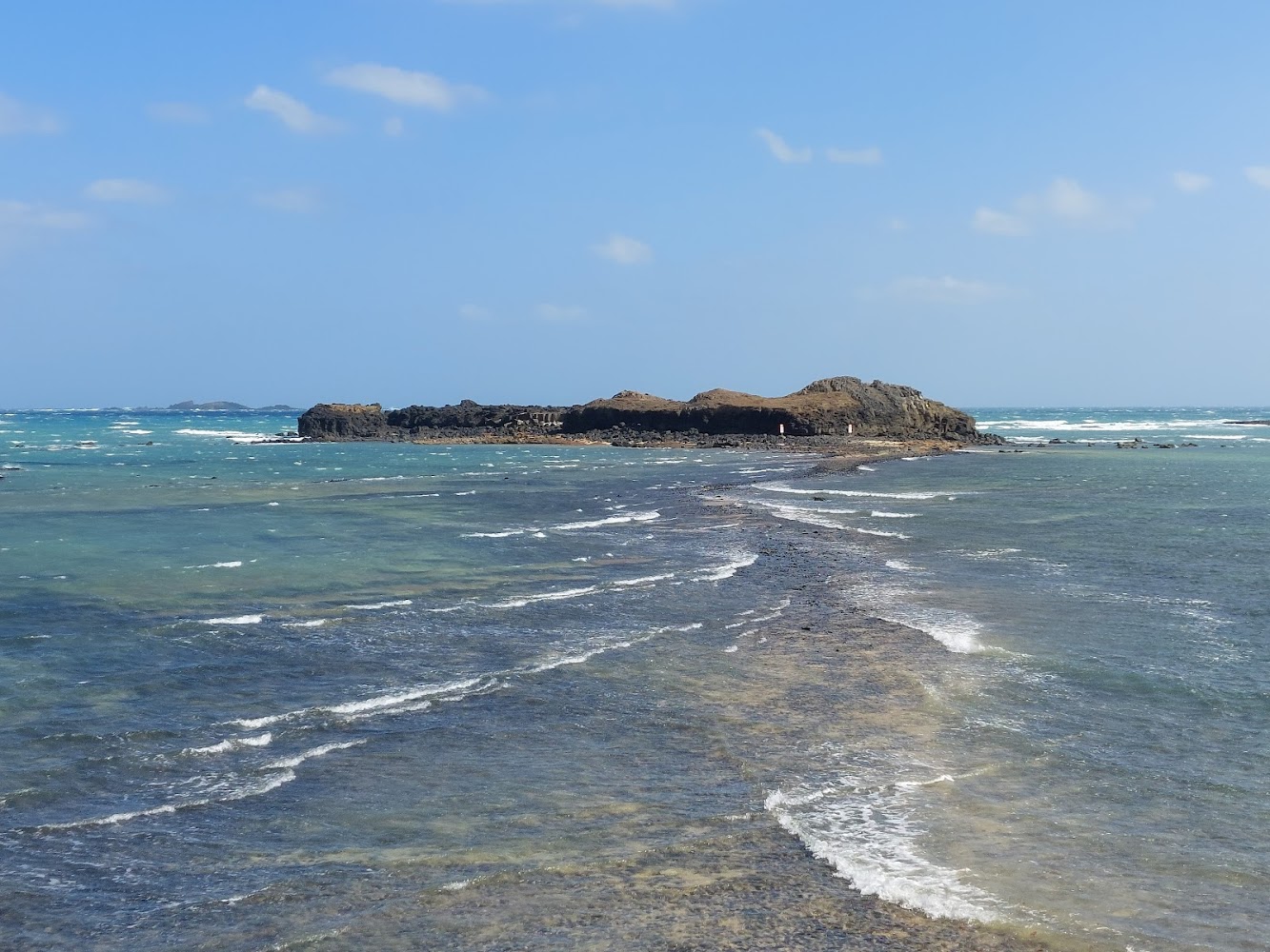 海中小島與岸邊間浮現石灘步道，海水藍綠清澈。