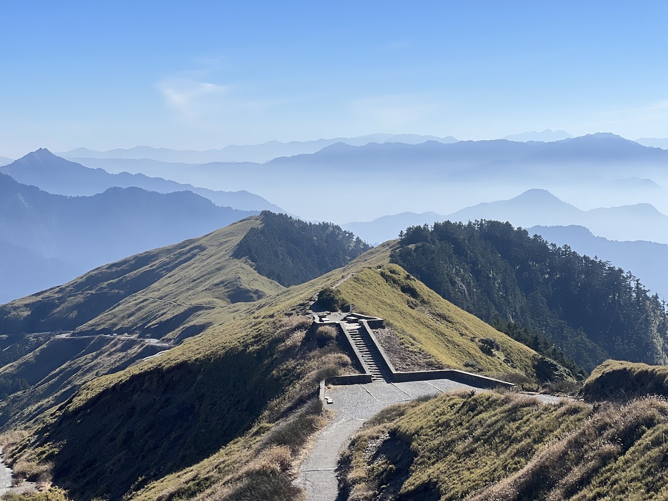 這張圖片主要呈現壯麗的山脈景色,山稜線上有蜿蜒的步道與階梯,遠處有層層山巒與清澈藍天,看不到明顯浮水印。