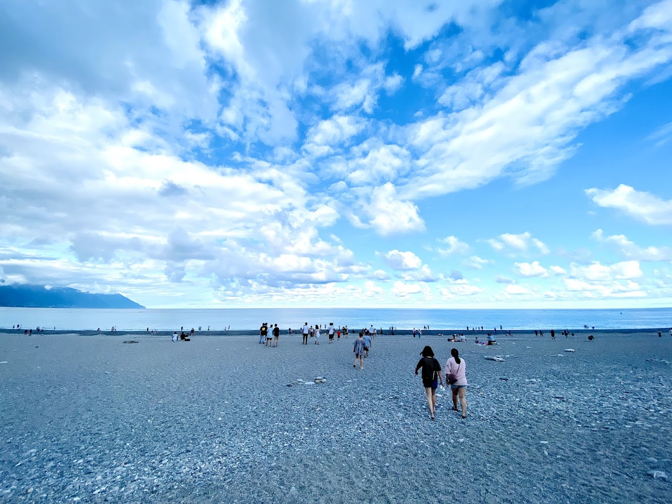 廣闊海灘上有遊客散步休憩，遠方可見山海相接