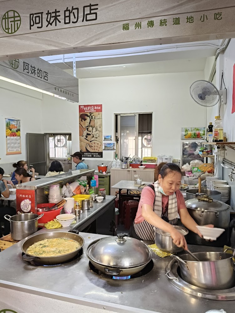 這張圖片主要展示一家名為『阿妹的店』的福州傳統小吃餐廳，畫面中有一位女性在廚房區域煮食，前方有多個鍋具，背景可見顧客用餐，氛圍溫馨樸實。