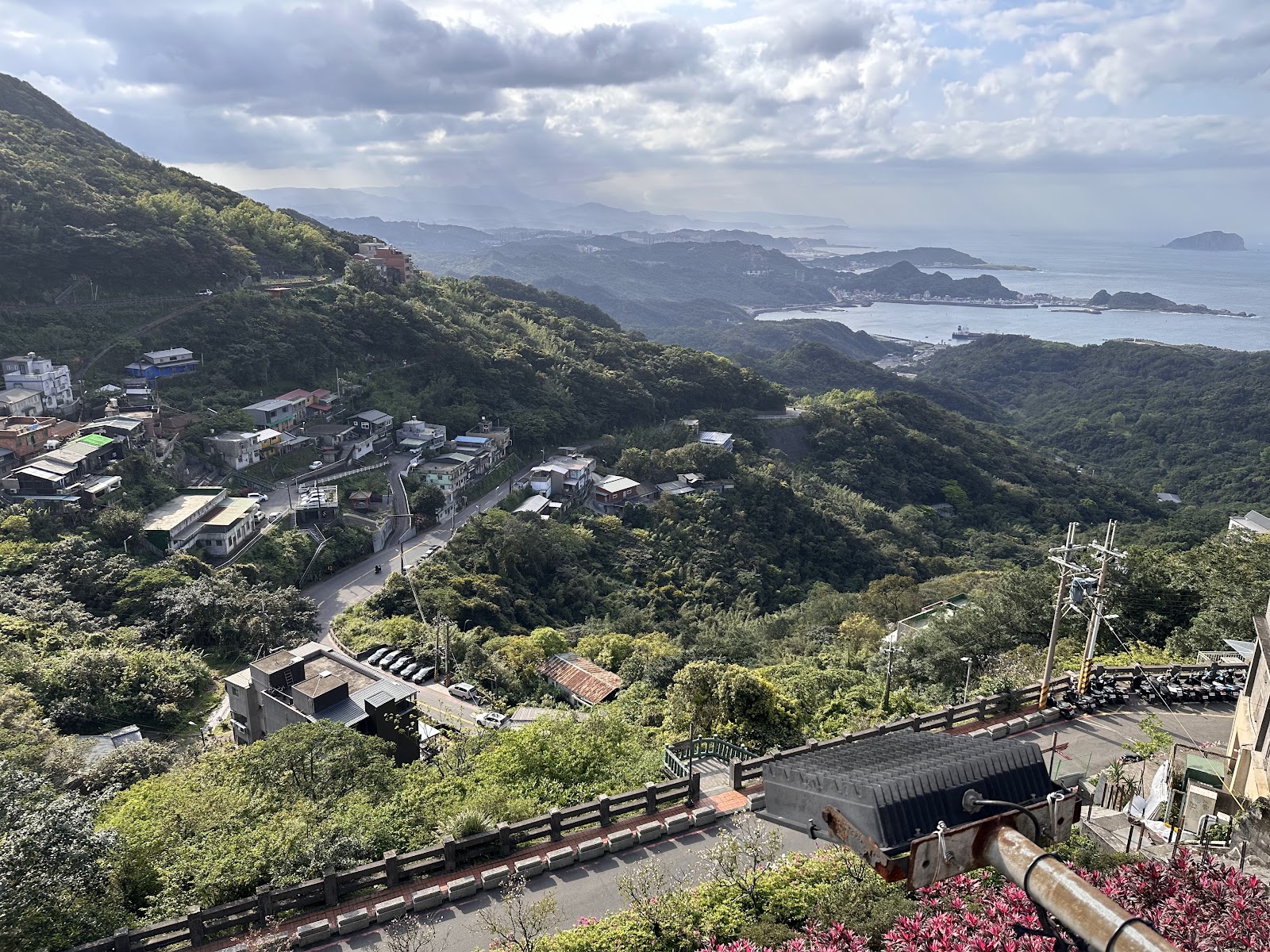 九份山頂俯瞰全景，山谷綠意，遠方基隆嶼，蜿蜒山路，雲霧繚繞
