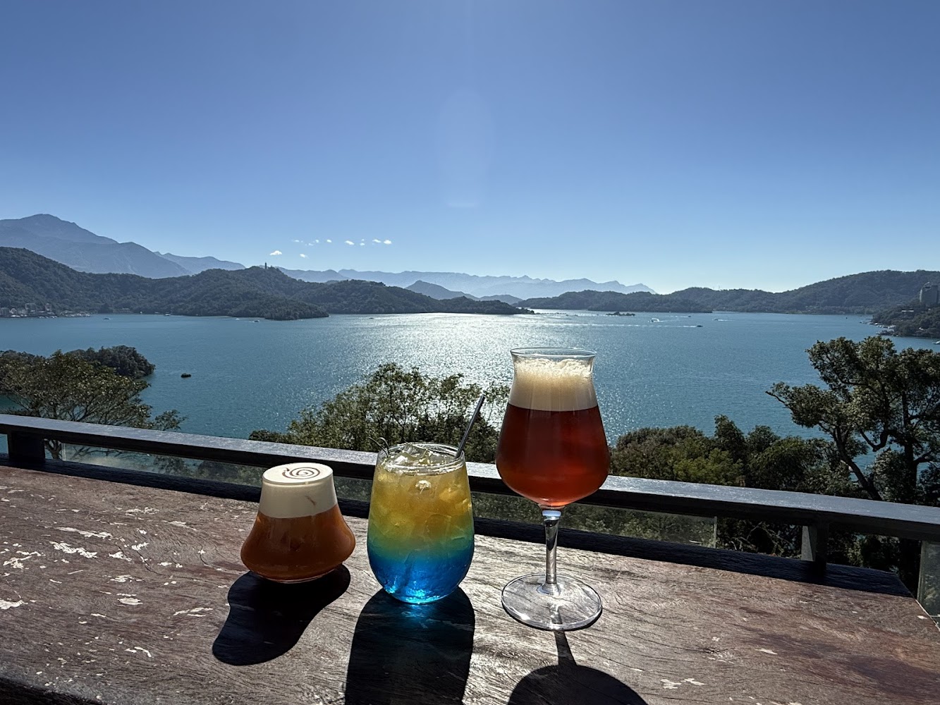 三杯飲品與晴朗湖景山景的悠閒桌面畫面