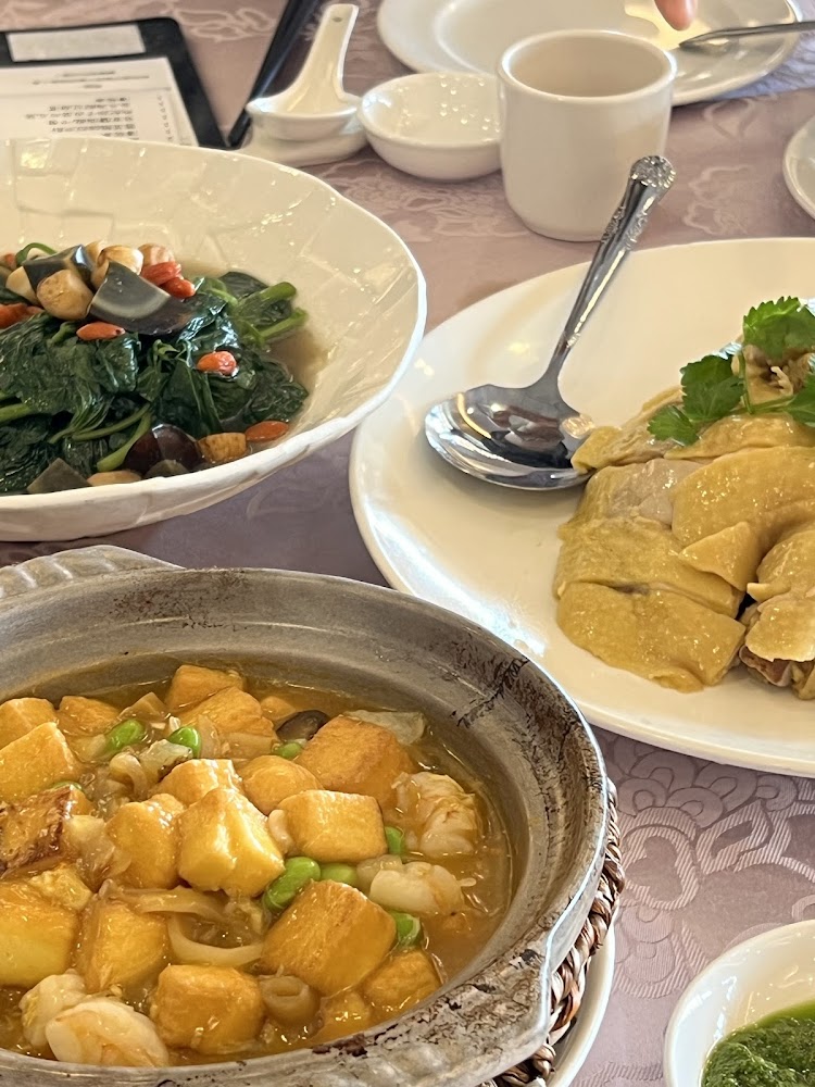三道中式菜餚:白切雞、豆腐煲和清炒蔬菜,桌上擺有餐具與茶杯