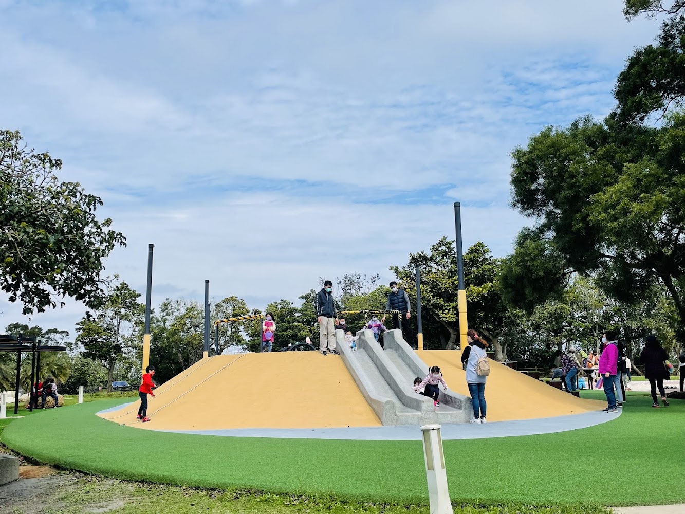 戶外公園遊樂場有黃色小山丘和數條溜滑梯小朋友正在遊玩