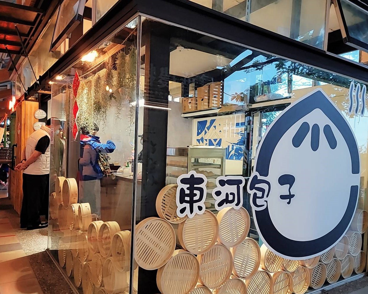 纏記舊街東河包子品牌牆面，紅色背景搭配大型包子吉祥物卡通