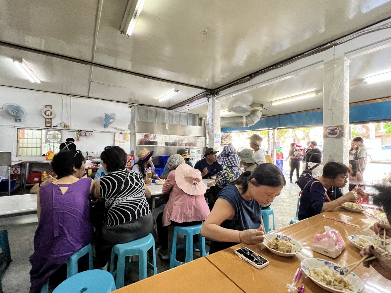 熱鬧的台灣小吃店內部，許多顧客坐在藍色椅子上用餐