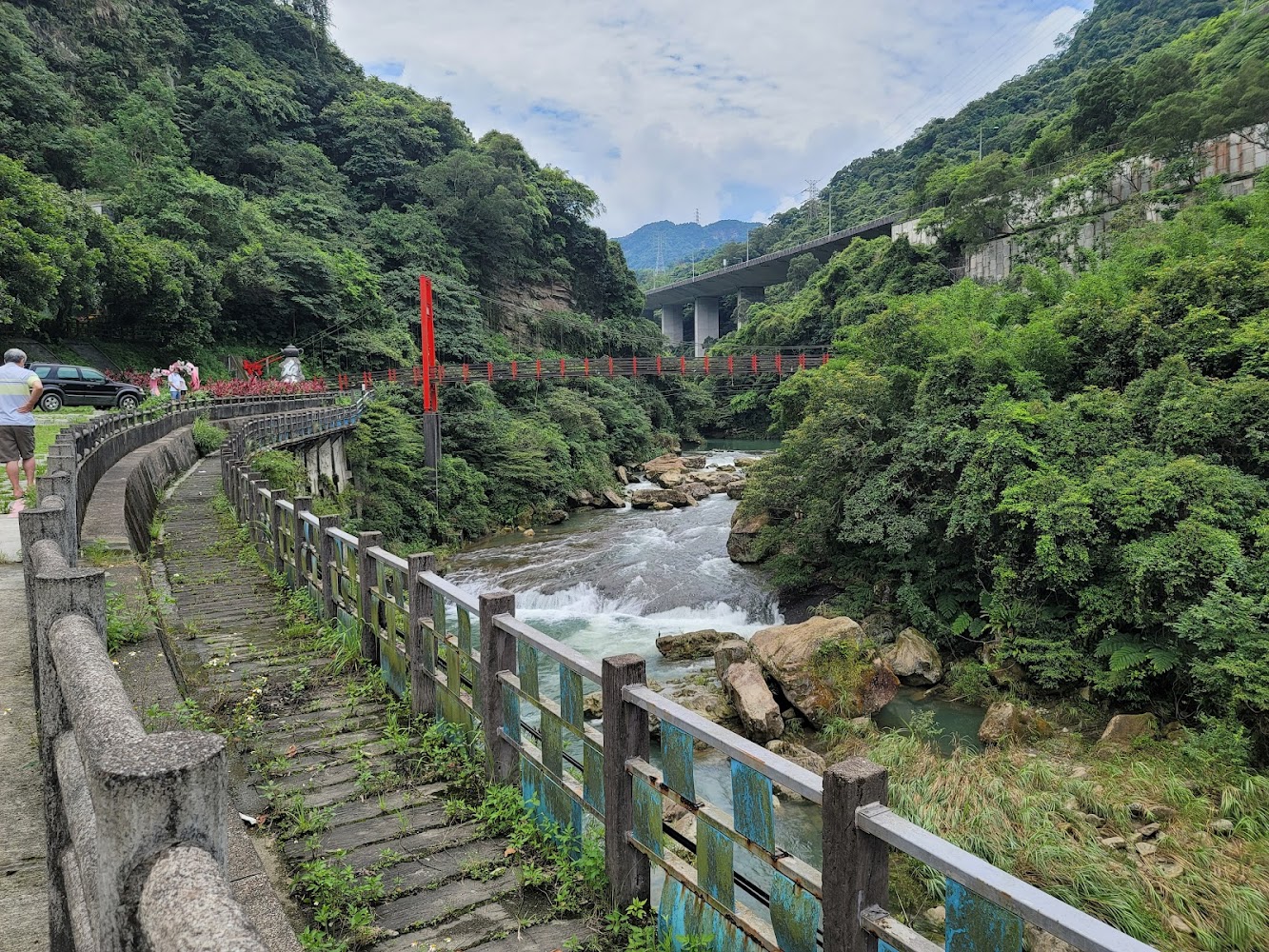 蜿蜒人行步道、溪流、巨石與紅色吊橋構成山林景觀