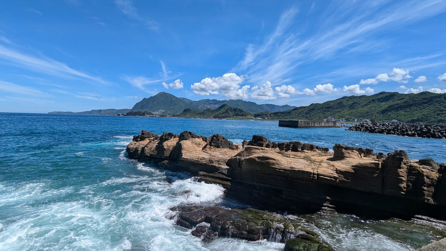 碧藍海水與奇岩怪石，遠方有青山