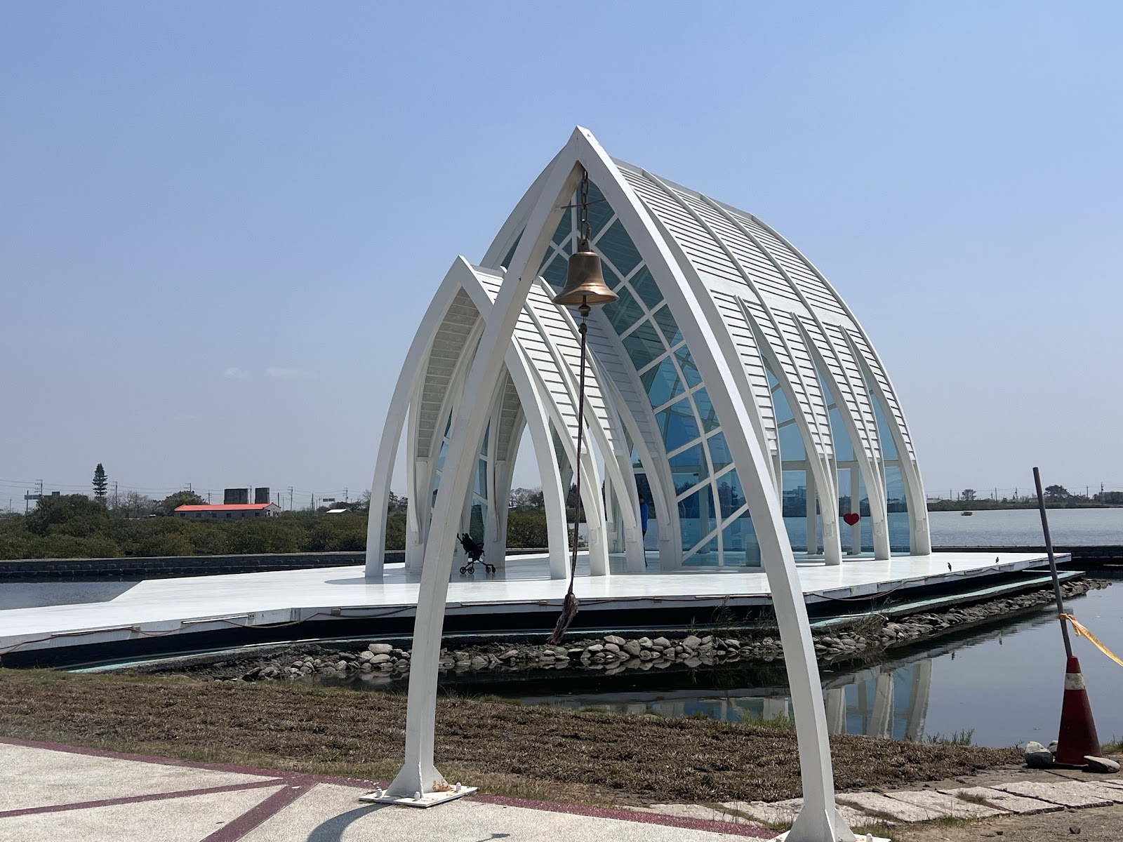 北門水晶教堂全景，白色弧形鋼架水上建築，銅鐘前景，晴天