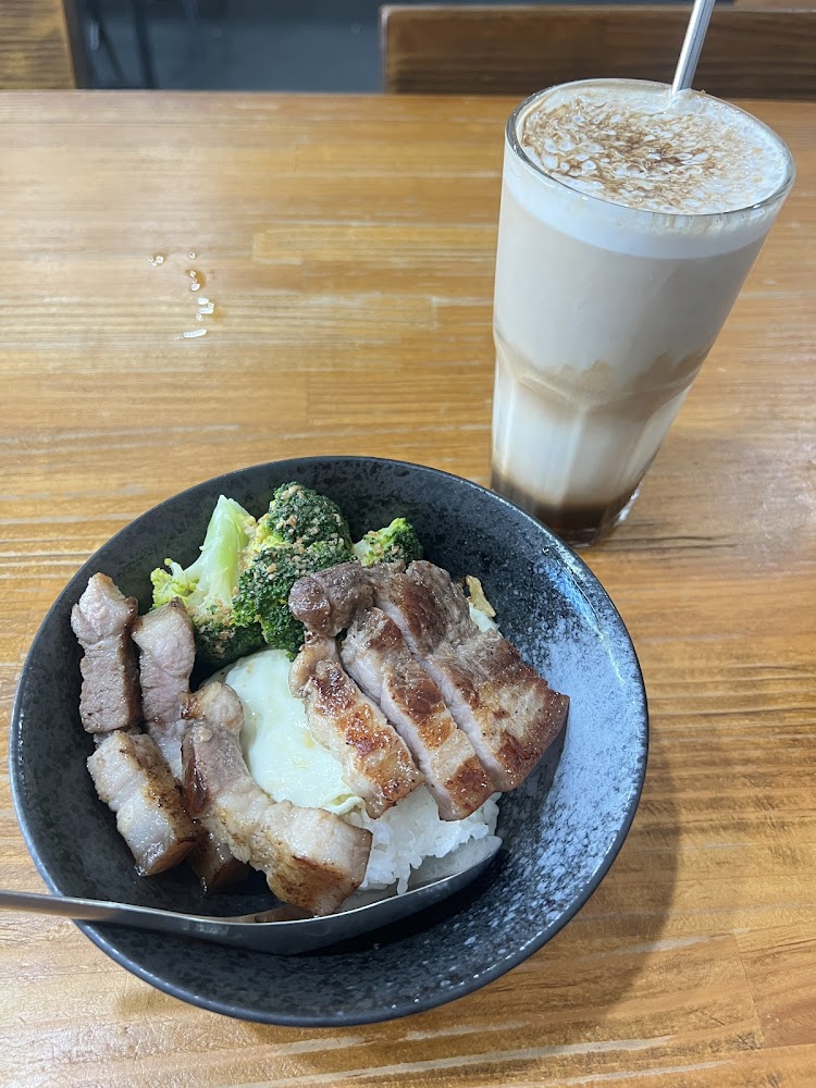 白飯上層有煎豬肉、花椰菜及荷包蛋，旁邊是一杯奶泡飲料
