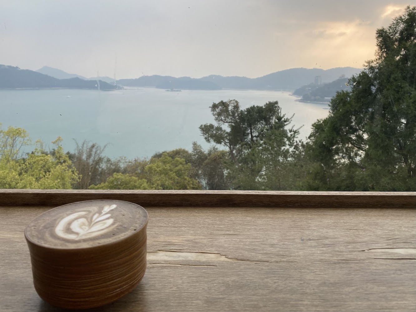 窗外湖泊遠山與夕陽景色前的一杯拉花咖啡
