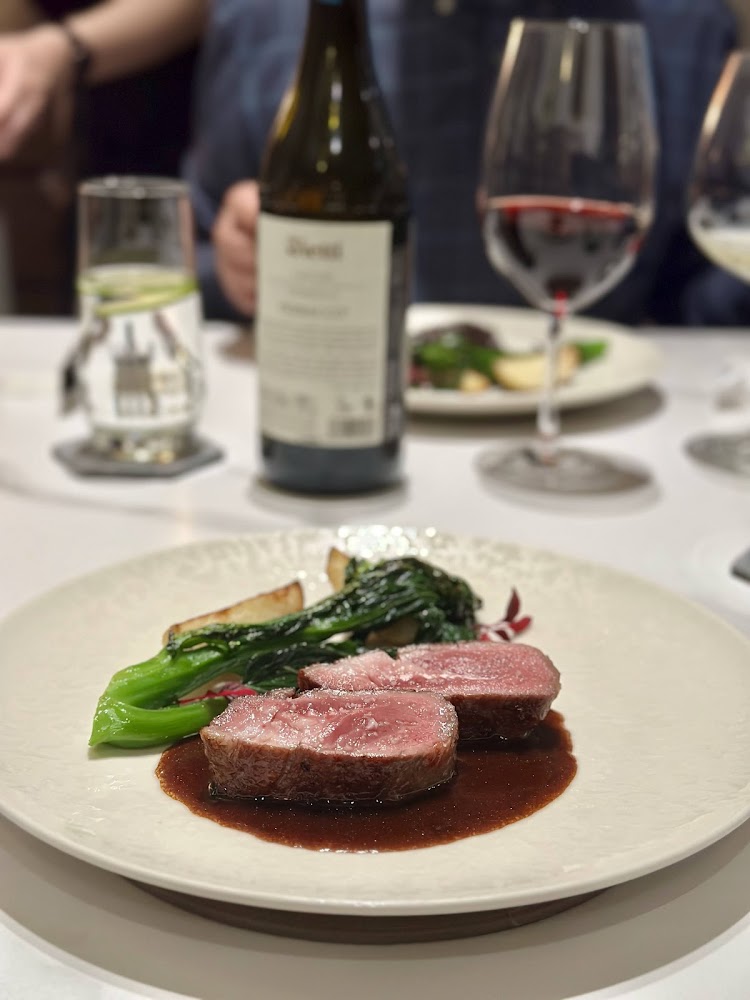 牛排主菜搭配醬汁、蔬菜與馬鈴薯，桌上有紅白酒與水杯