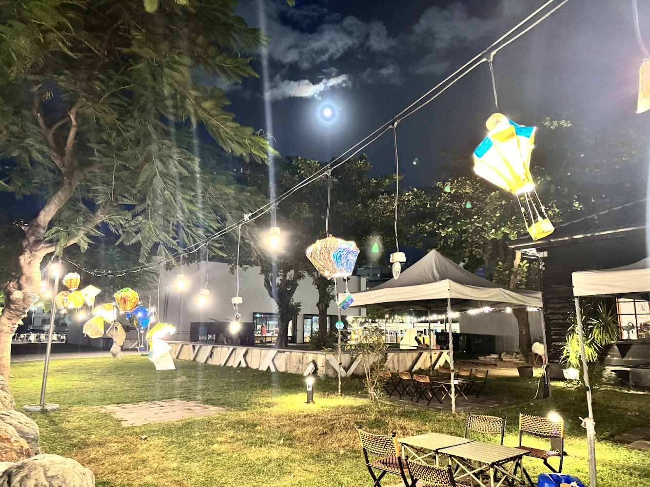 夜晚草地上掛著熱氣球燈籠與帳篷桌椅，月亮高掛