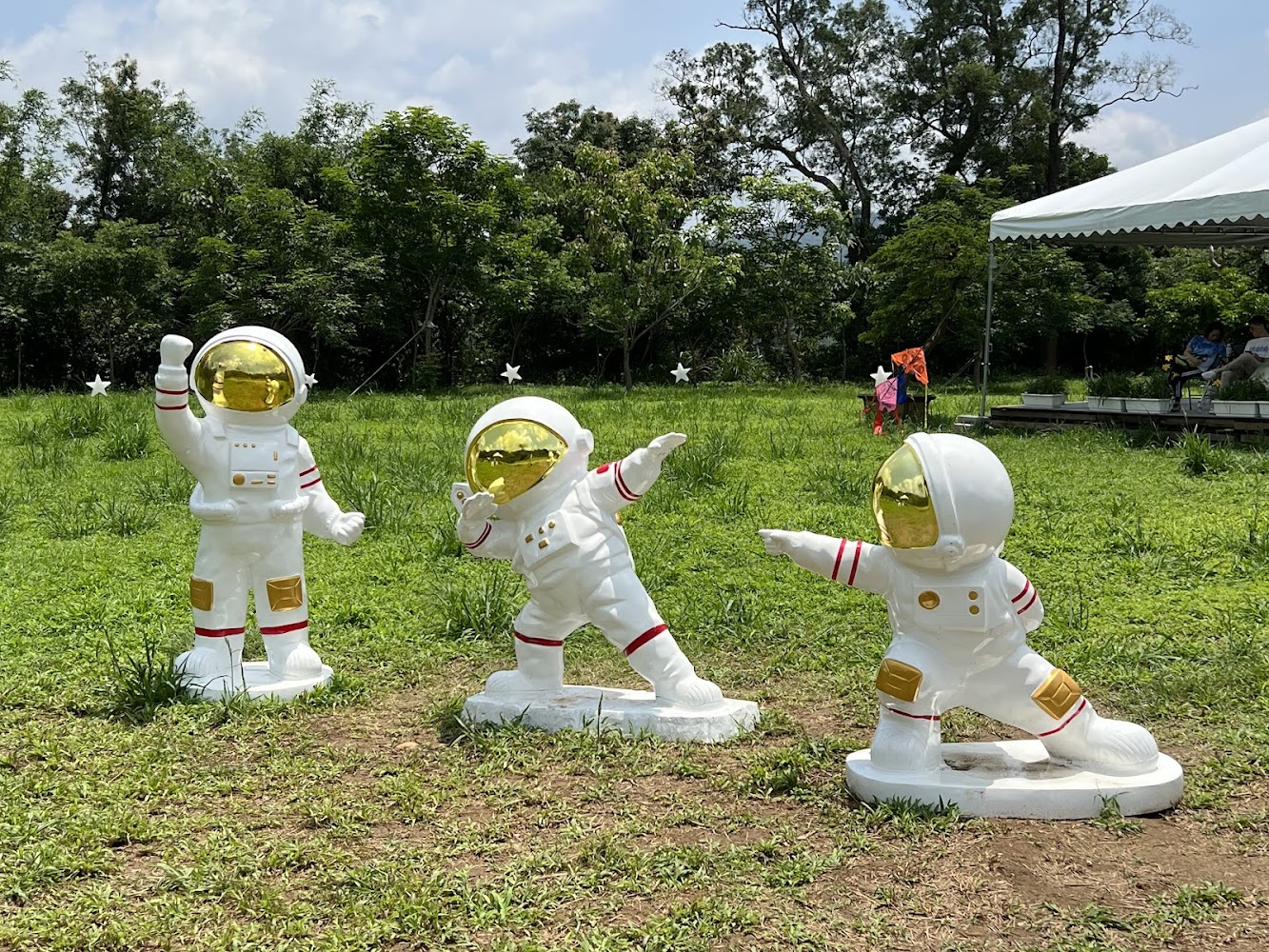三個可愛的太空人公仔雕像穿著白色太空服,背景是綠色草地和樹林
