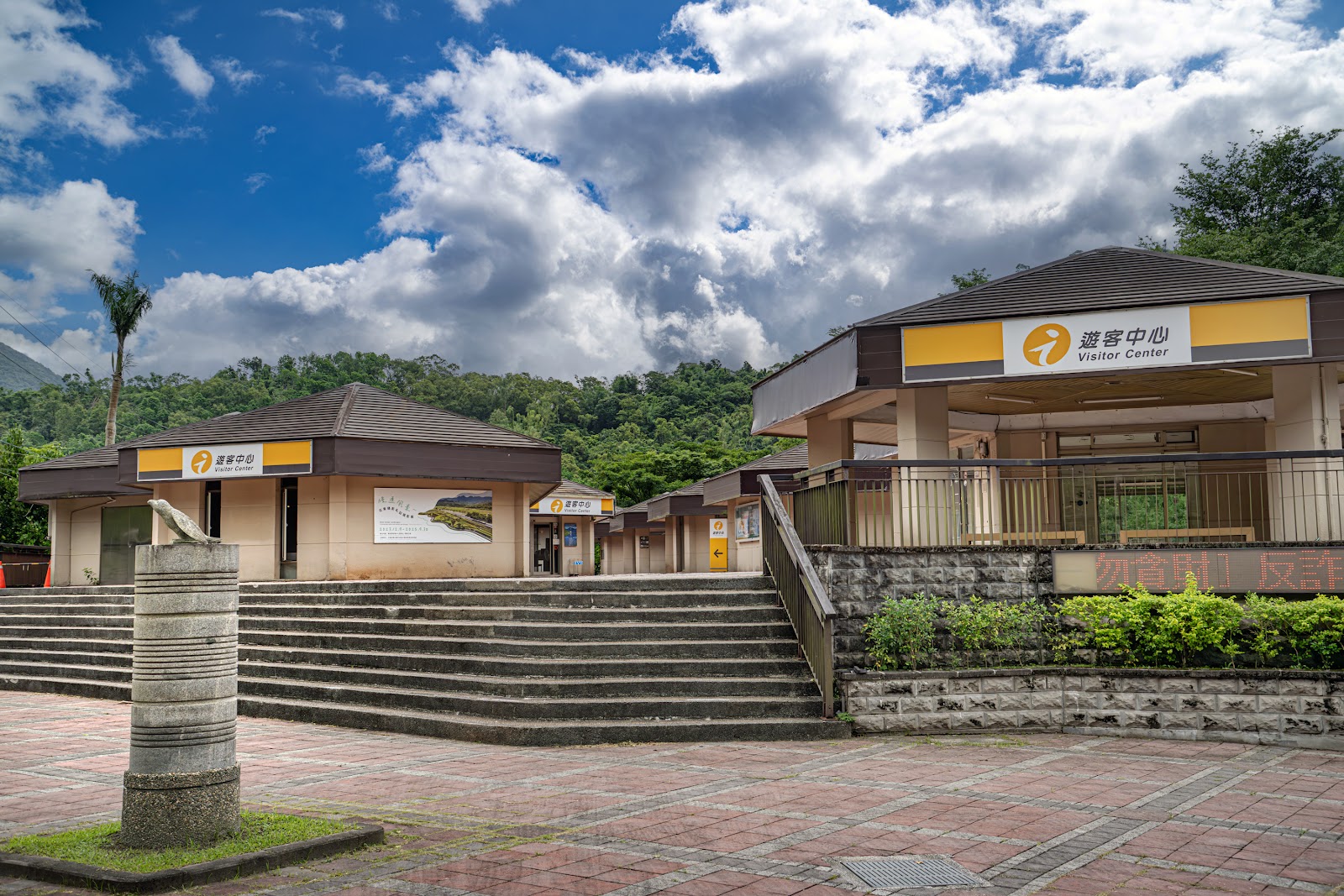 鯉魚潭遊客中心外觀，黃色招牌建築，藍天白雲背景，廣場寬闊