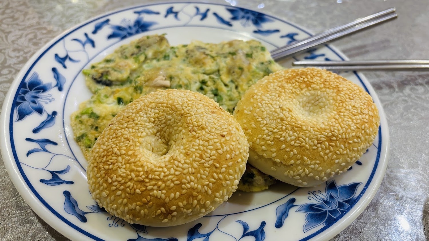 這張圖片展示了一盤美味的中式早餐，有兩個灑滿芝麻的燒餅，以及一塊蔥蛋，旁邊還放有筷子，整體擺盤精緻可口。
