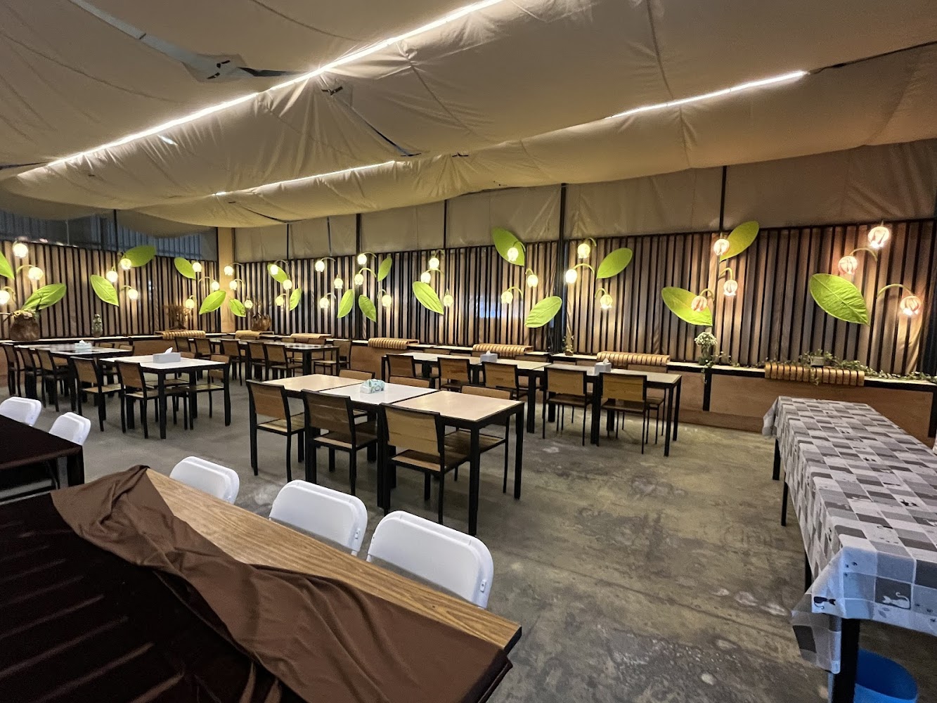 寬敞餐廳內有多張方桌與椅子牆面有燈泡和綠葉裝飾