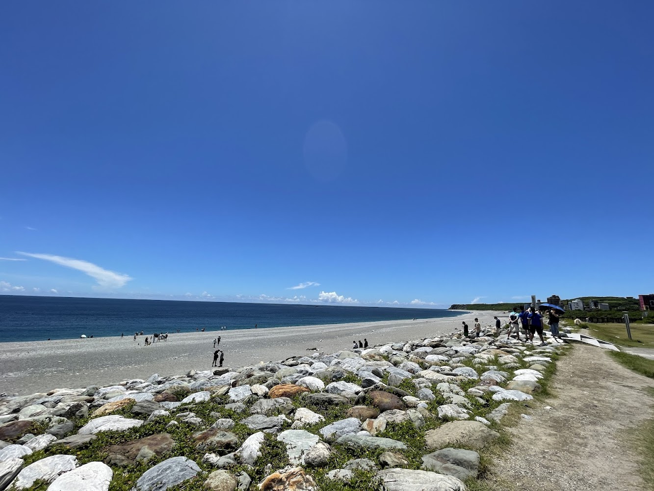 海灘前景有許多大石頭，遠方有遊客活動的七星潭景象