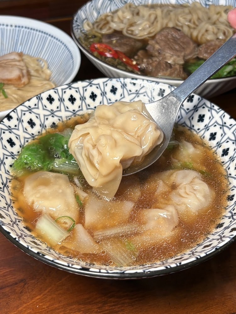 餛飩湯近拍，碗中有餛飩與青菜，後方可見其他麵食