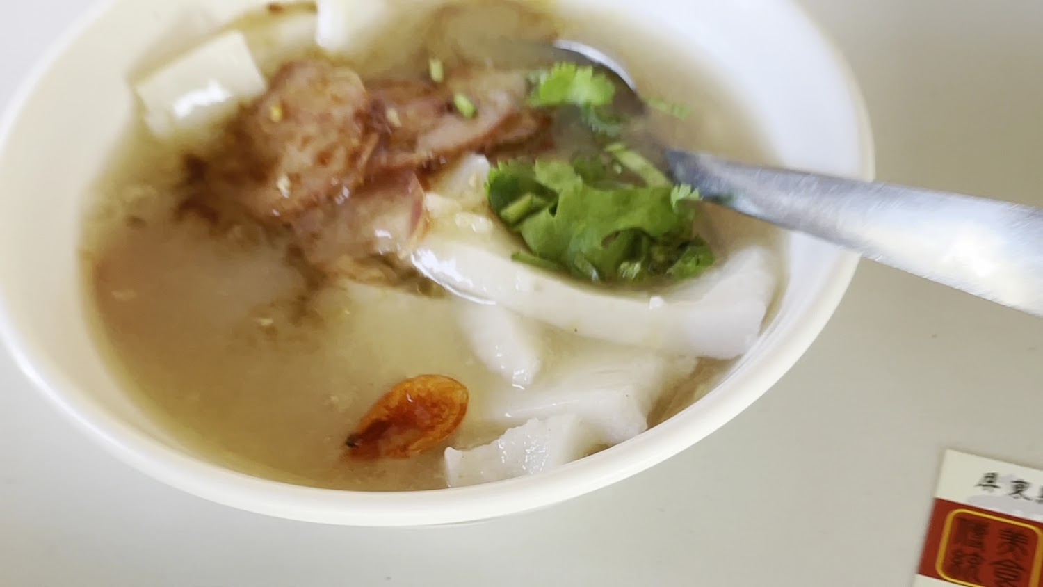 一碗清淡湯底的米苔目湯，上有香菜與肉片