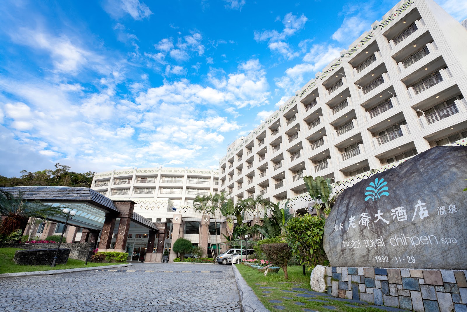 知本老爺酒店外觀，白色多層樓建築配合石碑招牌「知本老爺大酒店 溫泉」，前方為鵝卵石廣場及熱帶植栽