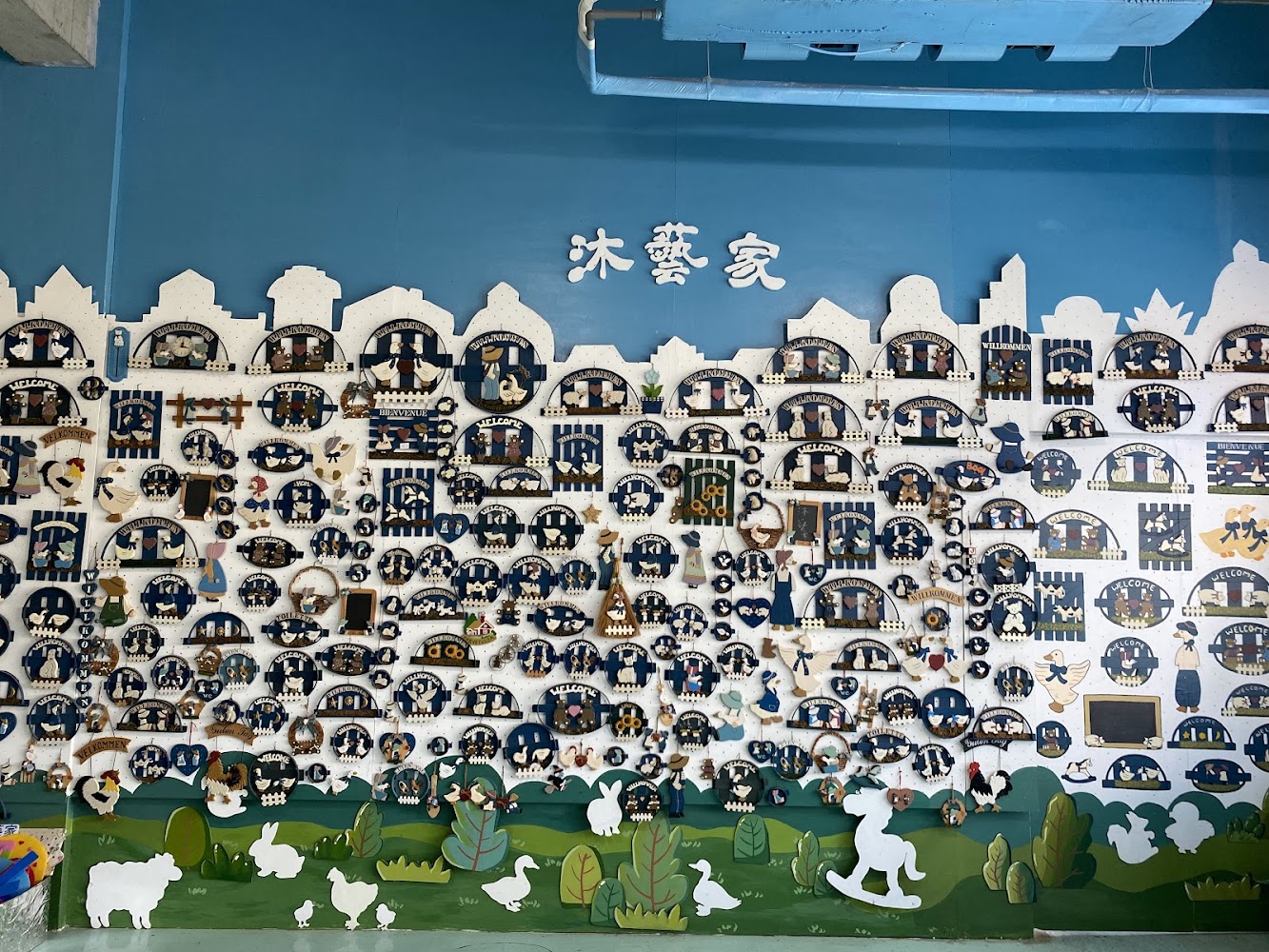 藍色牆面裝飾著許多以WELCOME與動物主題為主的小木牌，牆上還有沐藝家的字樣和綠色草地剪影。
