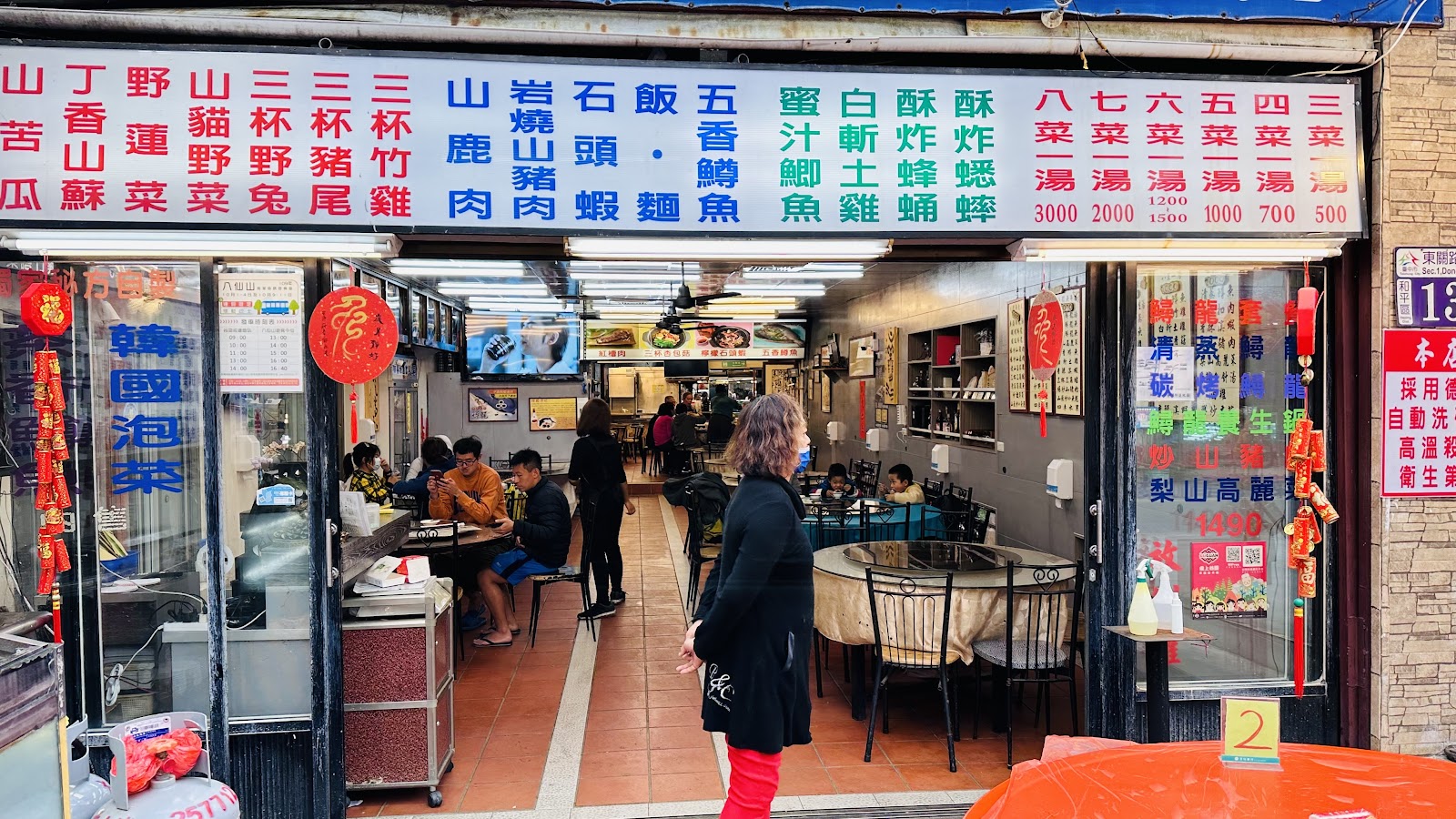 金谷餐廳外觀,上方招牌列滿山產菜色,室內圓桌圓椅,客人用餐中