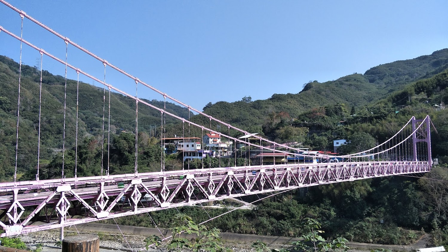 粉紅色吊橋橫跨山谷周圍是青綠山丘