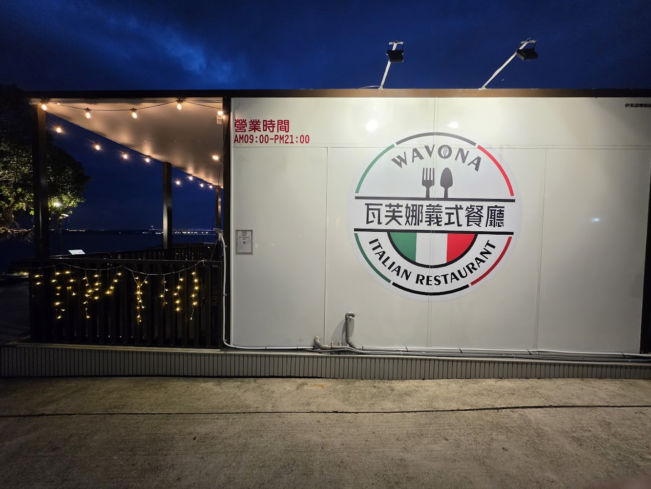 這張圖片展示了家名為瓦芙娜義式餐廳的店面，門口有營業時間標示和圓形標誌，旁邊還有燈飾點綴，營造溫馨氛圍。