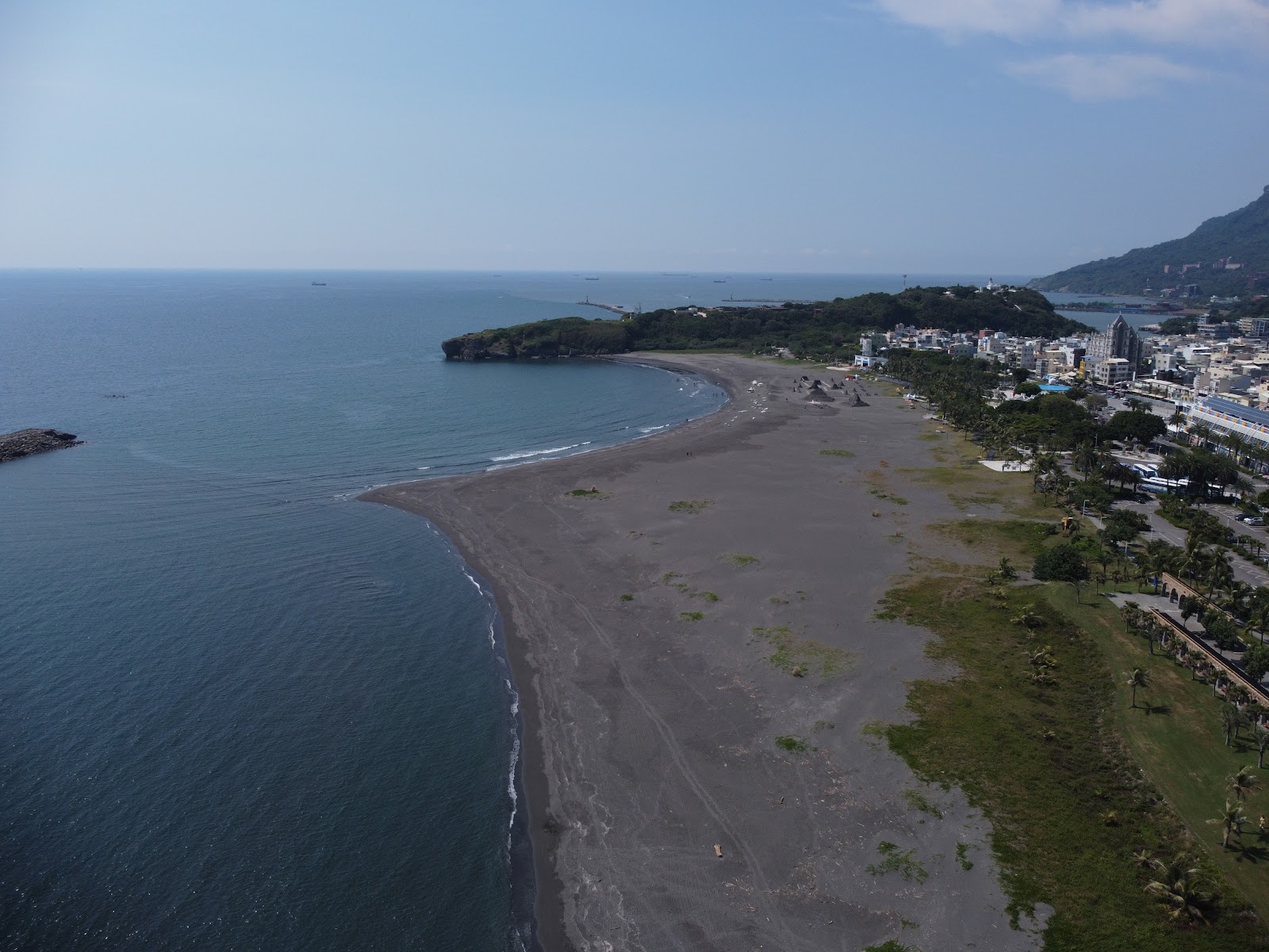 空拍俯瞰旗津海水浴場黑沙灘全景，弧形海灣，深藍色大海