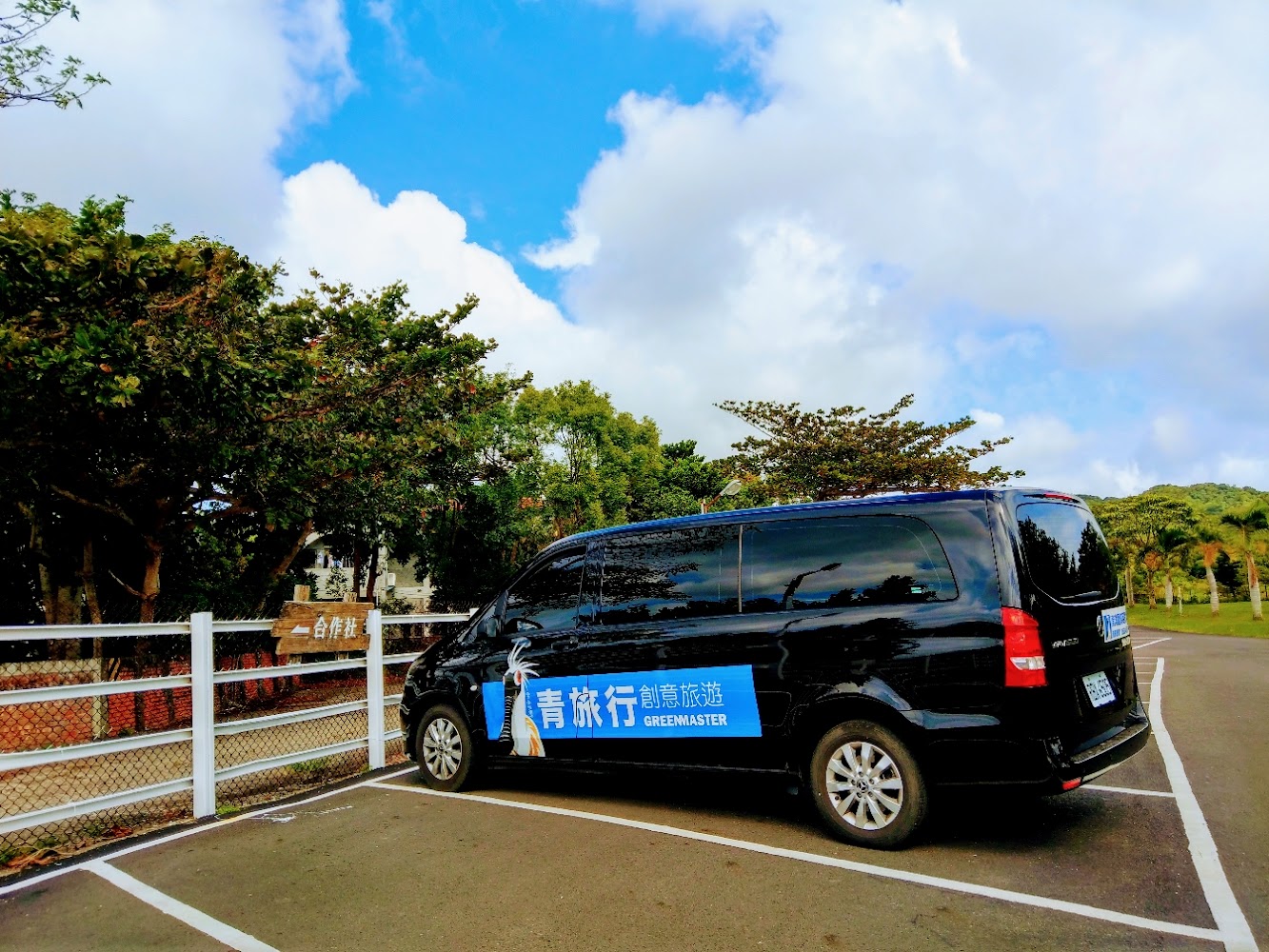 停車格內的黑色廂型車，車側貼有青旅行創意旅遊 GREENMASTER 標語