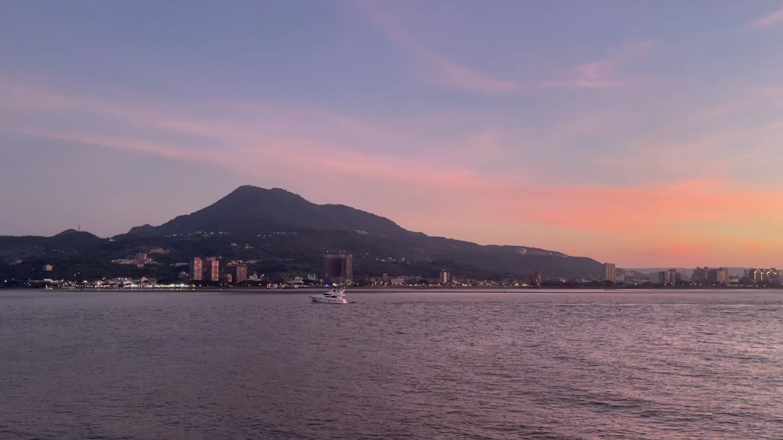 淡水河夕陽，觀音山剪影，遊艇行駛，橘紅天空倒映河面