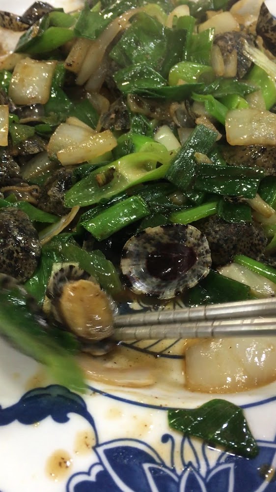 這張圖片主要是一盤炒海螺片搭配大量青蔥和洋蔥，食材色澤鮮亮，還有筷子夾著螺肉，呈現一道熱炒風味的海鮮料理。
