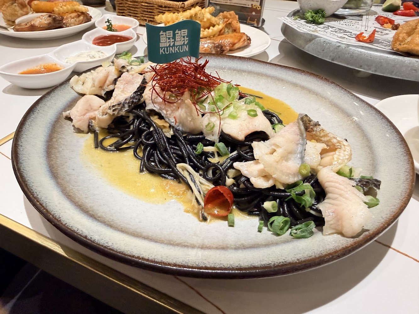 墨魚麵上鋪有魚肉香蔥與辣椒絲，旁邊搭配炸物拼盤
