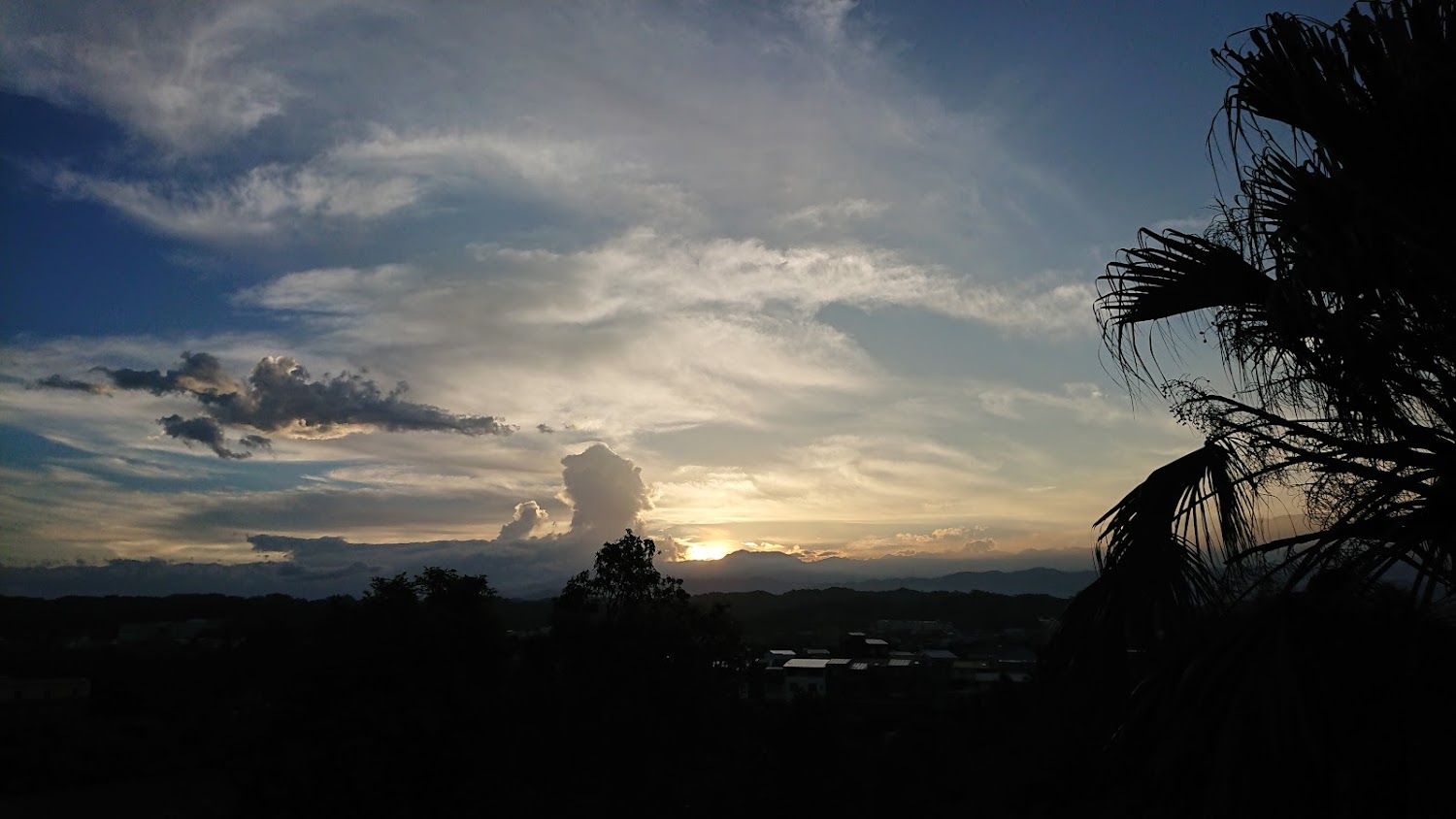 夕陽下的雲彩、山巒與房屋剪影