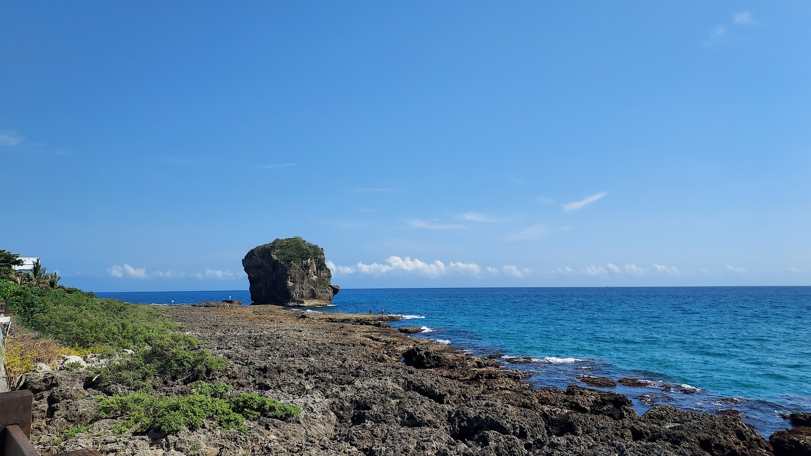 遠眺船帆石全景，奇岩矗立蔚藍海面，珊瑚礁岸線延伸，晴天藍海美景盡收眼底