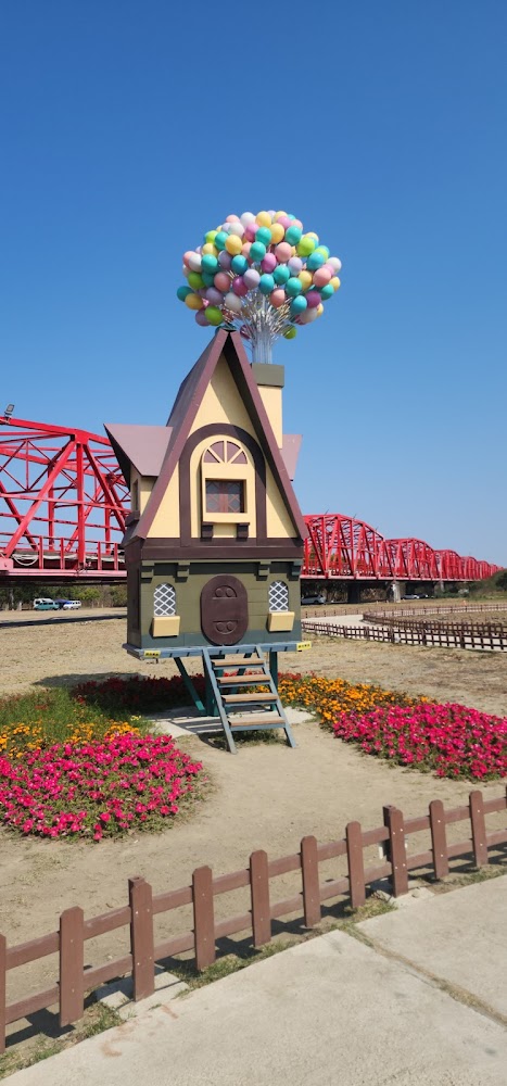 卡通風格小屋與彩色氣球裝飾，後方是紅色西螺大橋