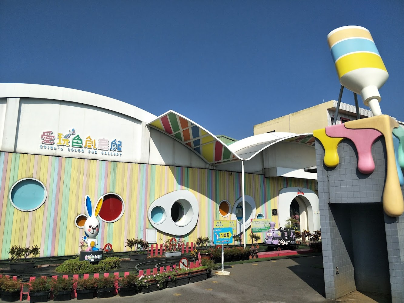 愛玩色創意館外觀，建築色彩繽紛，有大型調色瓶裝置和卡通兔子雕像，還有圓形窗戶與小火車，營造童趣氛圍。