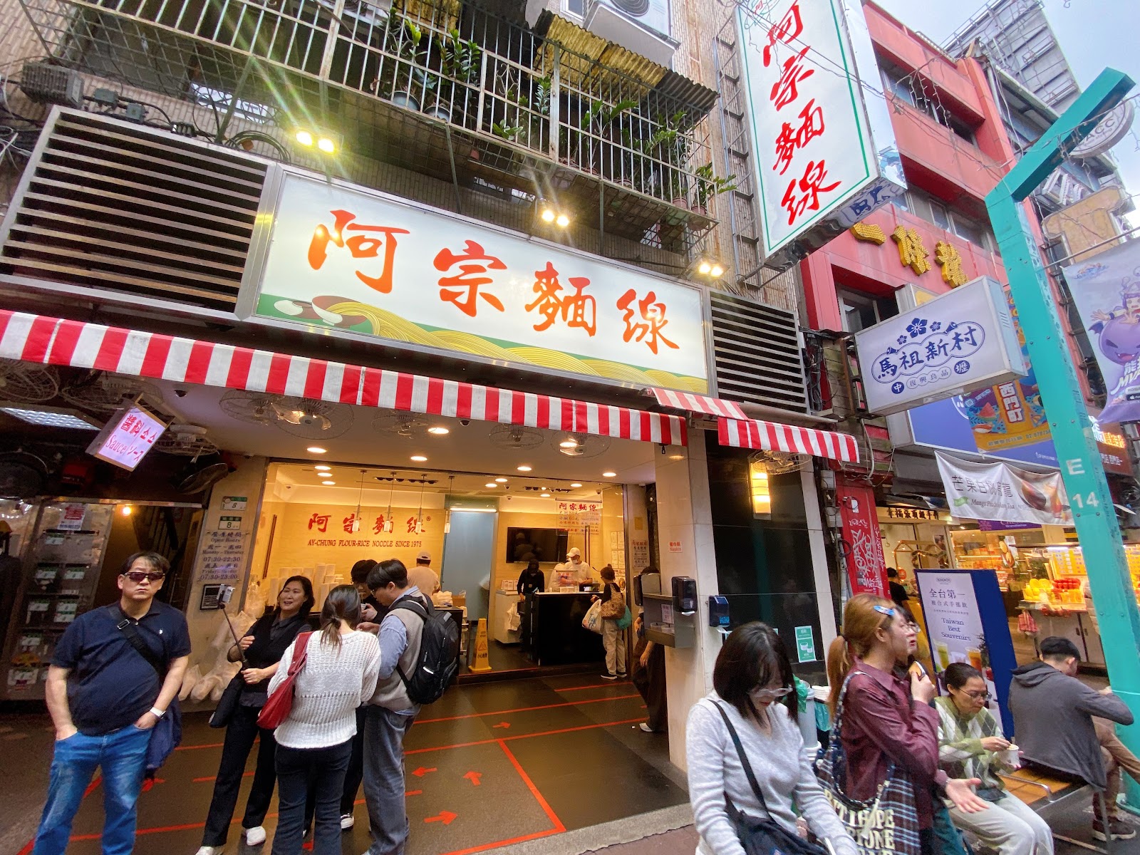 阿宗麵線店門外觀，紅白條紋遮陽棚，橙色大招牌，門口人潮排隊等候