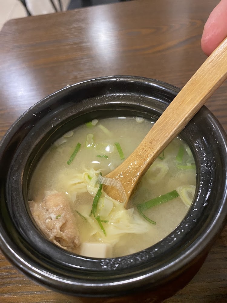 這張圖片顯示一碗味噌湯，裡面有豆腐、蔥花、湯匙及一些湯料，看起來熱騰騰且美味，是常見的日式料理湯品。