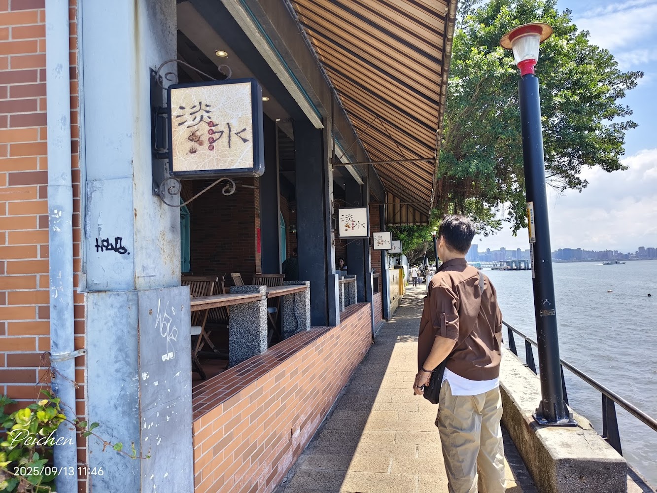 男子走在河邊步道旁，旁邊是一排磚牆餐廳，風景怡人
